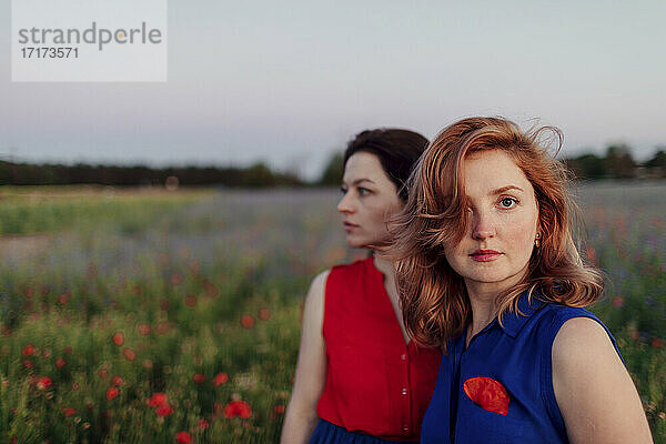 Mid adult woman standing with female friend in poppy field against sky