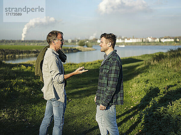 Father talking with son while standing on grass at riverbank