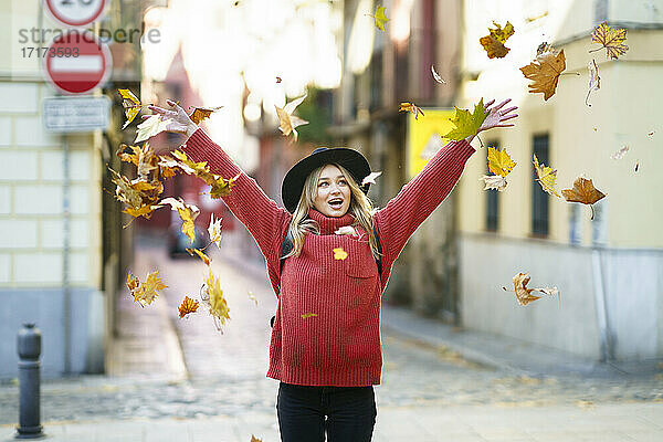 Carefree young woman throwing dry leaf while standing on street