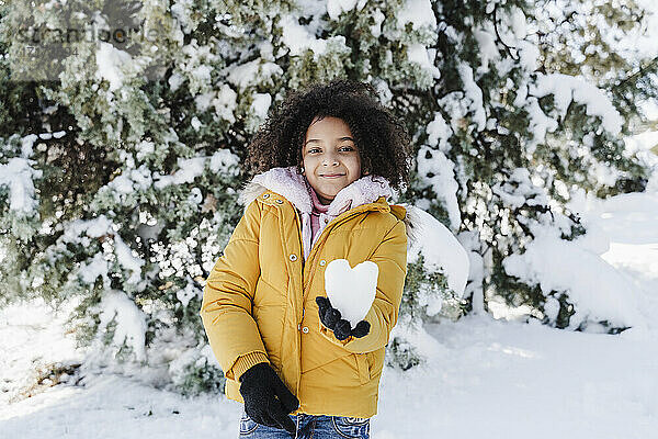 Lächelndes süßes Mädchen hält herzförmigen Schnee im Park