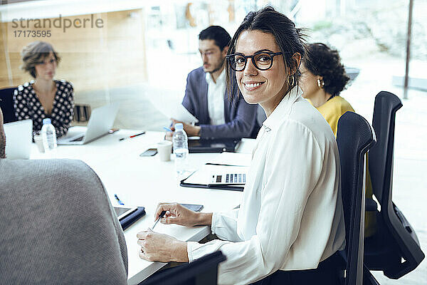 Lächelnde Geschäftsfrau  die mit ihren Kollegen im Sitzungssaal eines Coworking Centers sitzt