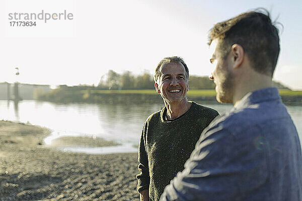 Happy father talking with son at riverbank on sunny day