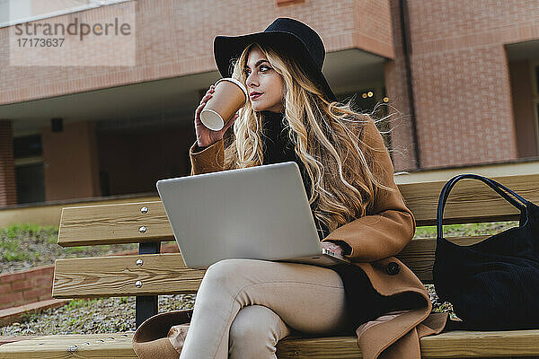 Woman with laptop drinking coffee while looking away