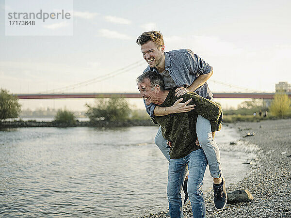 Happy father giving piggyback ride to son at riverbank
