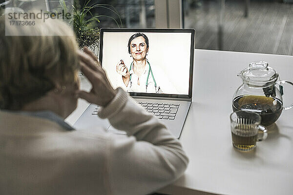 Ältere Frau lässt sich von einer Ärztin per Videoanruf im Wohnzimmer beraten