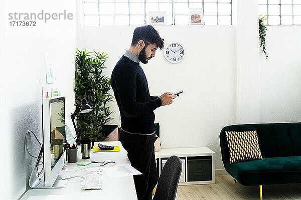 Geschäftsmann mit Smartphone am Schreibtisch im Büro stehend