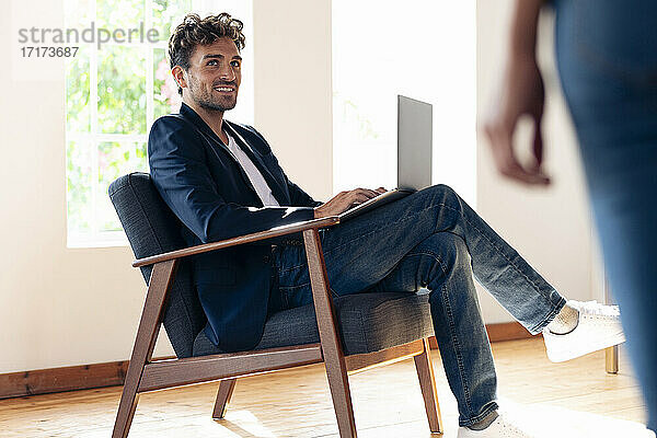 Lächelnder Geschäftsmann  der eine Frau ansieht  während er zu Hause am Laptop arbeitet