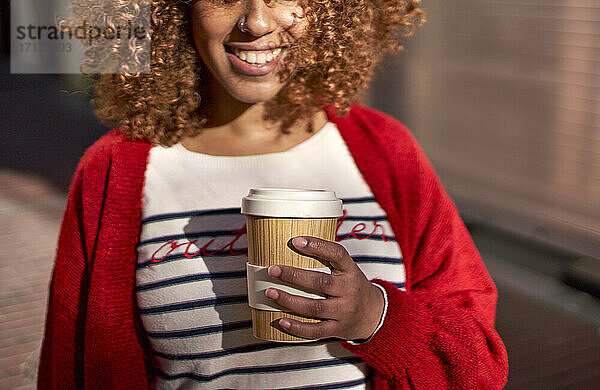 Smiling woman holding disposable coffee cup while standing outdoors