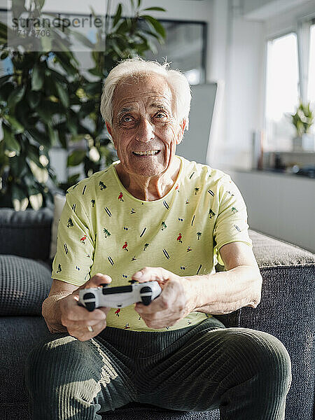 Älterer Geschäftsmann spielt ein Handheld-Videospiel  während er auf dem Sofa im Büro sitzt