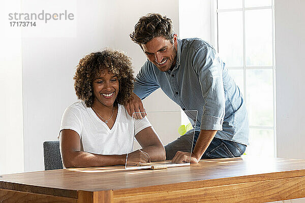 Mid adult couple smiling over transparent screen while sitting at home