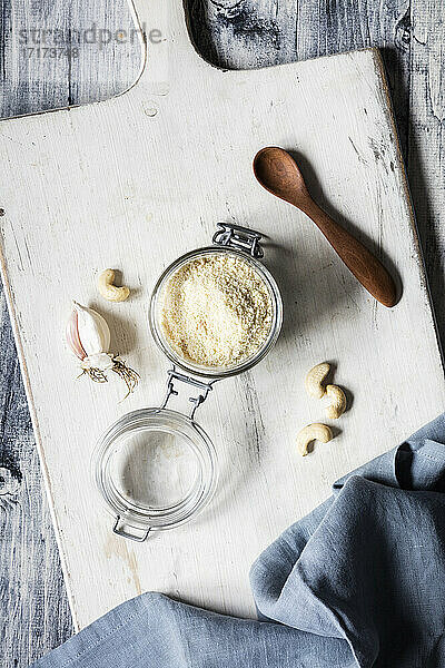 Cutting board with napkin  wooden spoon  garlic  cashews and jar of shredded vegan Parmesan cheese