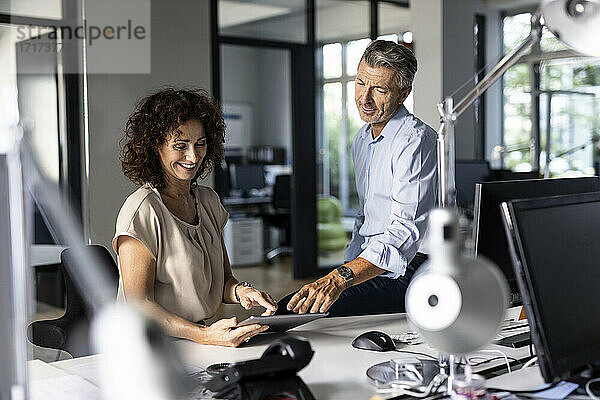 Geschäftsleute  die im Büro sitzend über ein digitales Tablet diskutieren