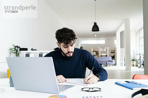 Junger Geschäftsmann schreibt am Schreibtisch in einem kreativen Büro