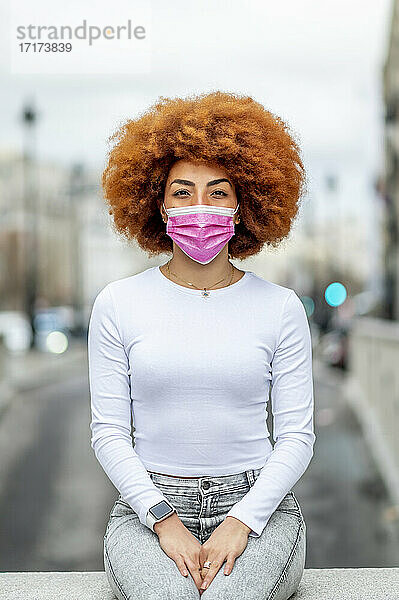 Mid adult woman wearing protective face mask while sitting on retaining wall