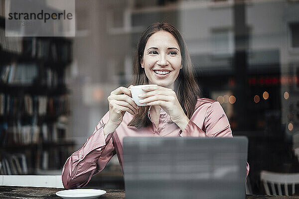 Lächelnde Unternehmerin  die in einem Café Kaffee trinkt und durch ein Glas schaut