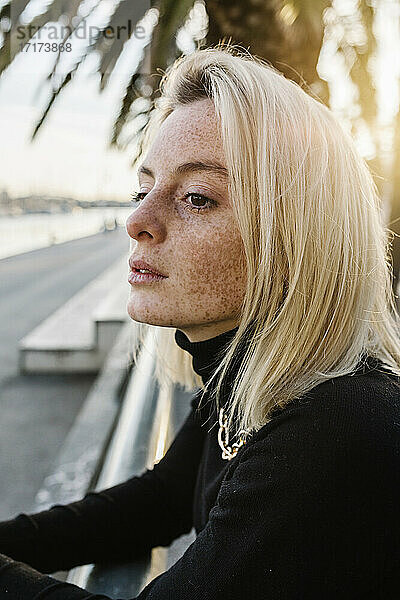 Young woman with freckles leaning on railing against palm tree