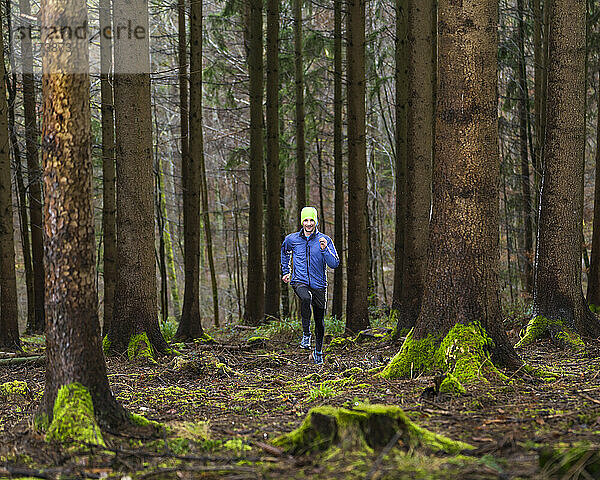 Junger Mann in blauer Jacke joggt im Wald