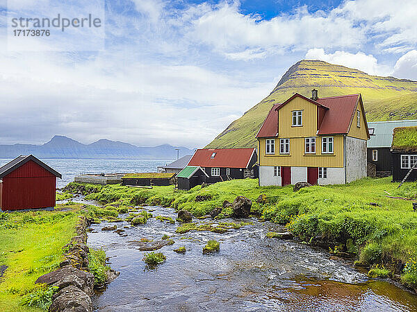 Stream flowing by houses against cloudy sky  Iceland