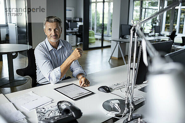 Älterer Unternehmer mit digitalem Tablet  der lächelnd im Büro sitzt