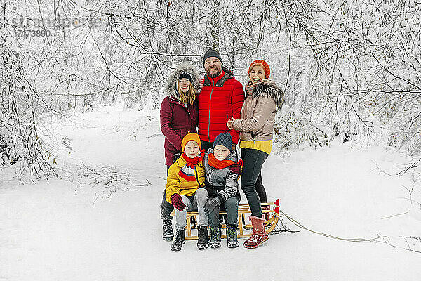 Lächelnde Eltern  die neben ihren Kindern stehen  die im Winter im Wald Schlitten fahren