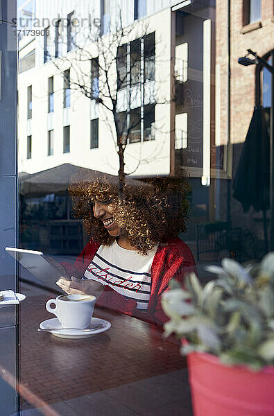 Young woman using digital tablet while sitting by window at cafe