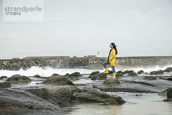 Frau betrachtet die Aussicht  während sie auf einem Felsen an der Küste steht