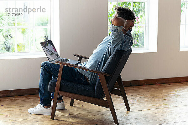 Mann mit Händen hinter dem Kopf  der sich zu Hause auf einem Sessel ausruht