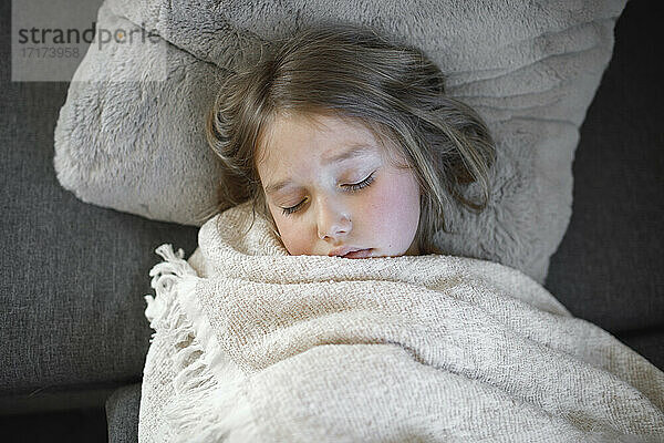 Krankes Mädchen schläft mit Decke auf Sofa zu Hause