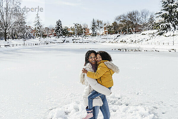 Lächelnde Mutter  die ihre Tochter trägt  während sie im Winter an Land steht