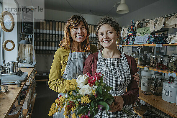 Ladenbesitzer mit einer Kollegin  die einen Blumenstrauß hält  während sie in einem Zero-Waste-Laden stehen