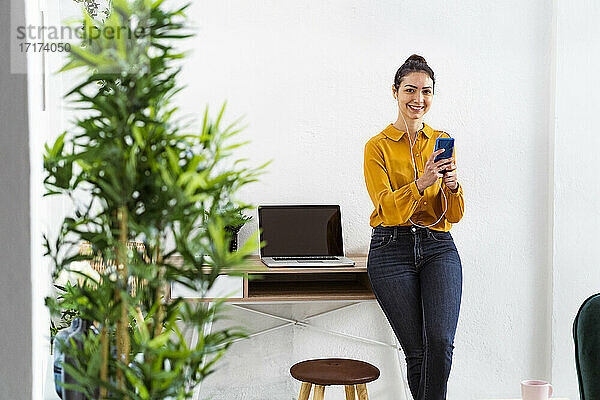 Smiling woman using smart phone while standing at home office