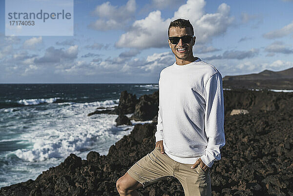 Lächelnder männlicher Tourist mit Händen in den Taschen auf einem Aussichtspunkt am Meer in Los Hervideros  Lanzarote  Spanien