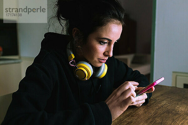 Junge Frau mit Kopfhörern  die auf ihr Telefon schaut