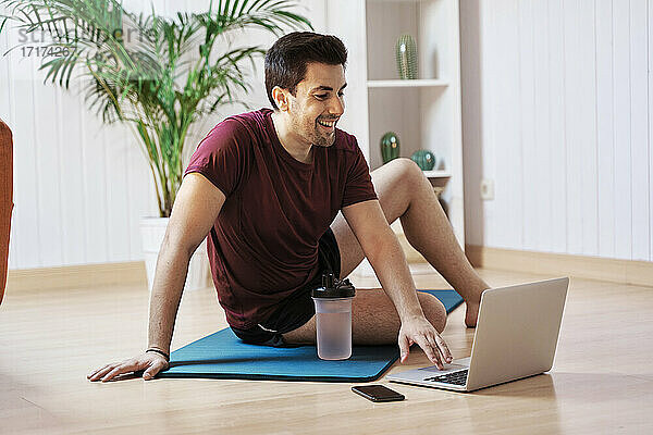 Mann auf Trainingsmatte zu Hause  mit Laptop