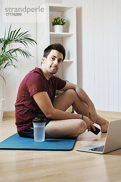 Mann zu Hause mit Trainingsmatte und Laptop