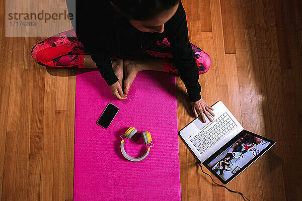 Junge Frau sitzt auf einer Yogamatte und führt ein Videogespräch über einen Laptop