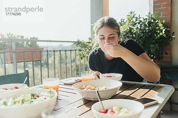 Junge Frau isst eine Mahlzeit auf dem Balkon