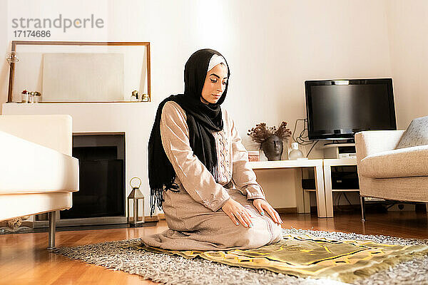 Junge muslimische Frau kniet zum Gebet auf einer Matte
