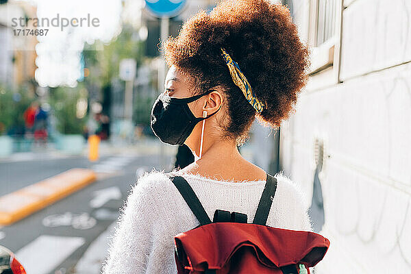 Junge Frau geht in der Stadt spazieren  trägt Gesichtsmaske  Rückansicht