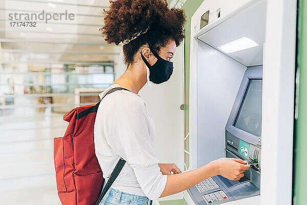 Junge Frau mit Gesichtsmaske  die einen Geldautomaten benutzt