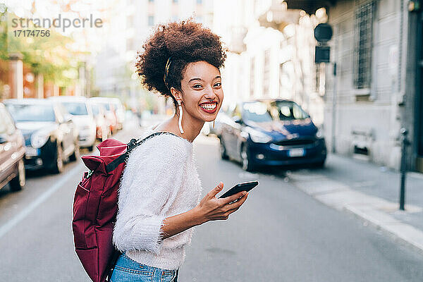 Junge Frau auf der Straße hält Telefon und lächelt