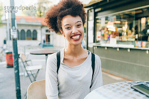 Junge Frau sitzt lächelnd am Tisch eines Cafés im Freien