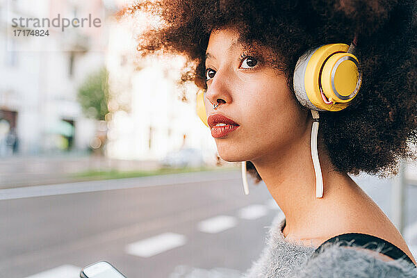 Junge Frau mit Kopfhörern  wegschauend  im Freien