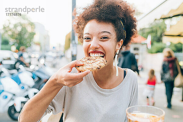 Junge Frau isst Keks in einem Straßencafé