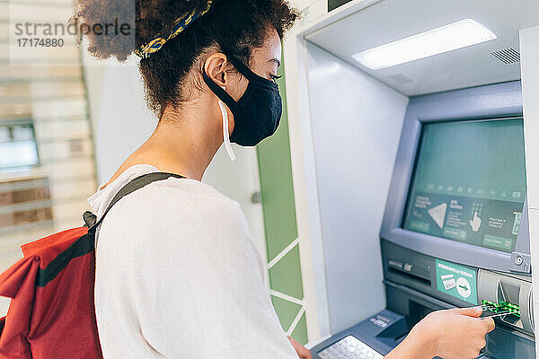 Junge Frau mit Gesichtsmaske  die einen Geldautomaten benutzt