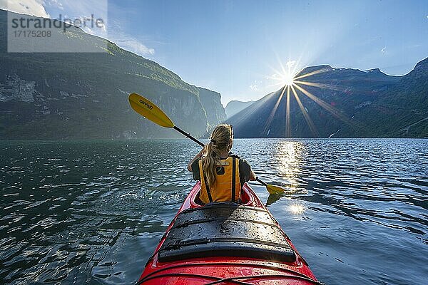 Junge Frau paddelt in einem Kajak  Sonne scheint  Geirangerfjord  bei Geiranger  Norwegen  Europa