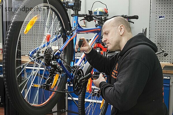 Zweiradmechaniker in der Fahrradwerkstatt während einer Inspektion an einem Mountainbike  Kontrolle und Einstellen der Schaltung