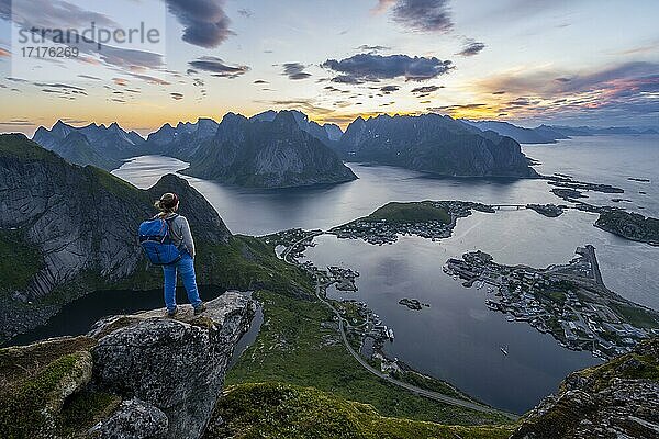 Abendstimmung  junge Wanderin steht auf Felsvorsprung und genießt Aussicht vom Reinebringen  Reinebriggen  Hamnoy  Reine und den Reinefjord mit Bergen  Moskenes  Moskenesöy  Lofoten  Norwegen  Europa