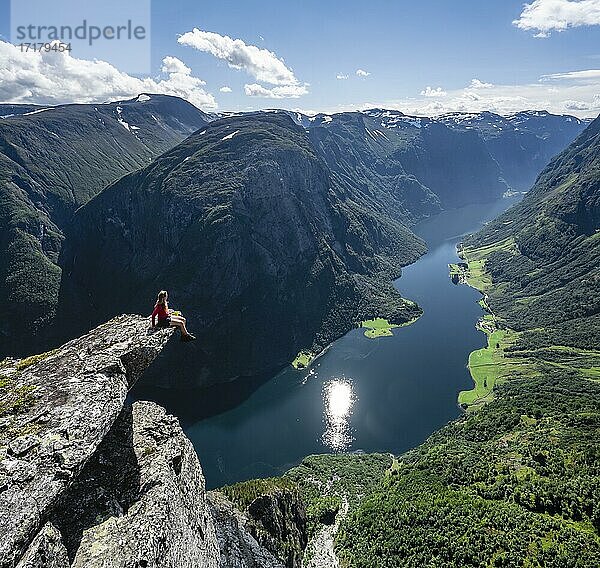 Wanderin sitzt auf Felszunge  Blick vom Gipfel des Breiskrednosi  Berge und Fjord  Nærøyfjord  Aurland  Norwegen  Europa
