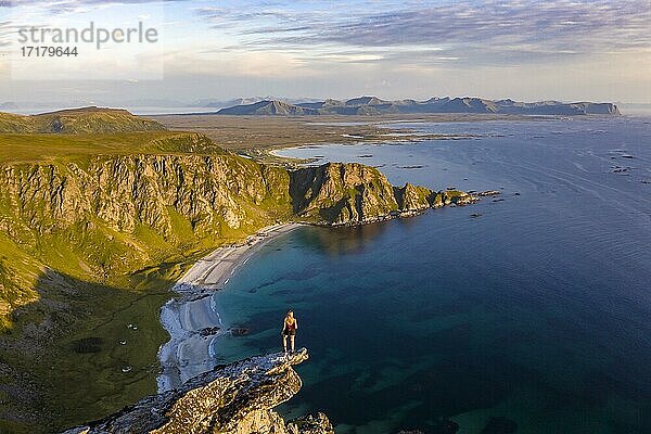 Abendstimmung  Wanderin steht am Abgrund auf Felsvorsprung  Blick auf Felsen  Strand und Meer  Gipfel des Berges Måtinden  bei Stave  Nordland  Norwegen  Europa